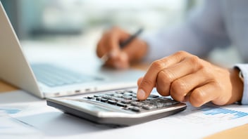 Mano de un profesional de RH usando una calculadora sobre un escritorio para realizar el cálculo de un finiquito o liquidación laboral.