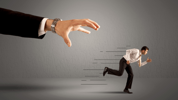 Hombre de negocios huyendo de una mano gigante que intenta atraparlo, simbolizando la fuga de talento y los desafíos en la retención de empleados en una empresa.