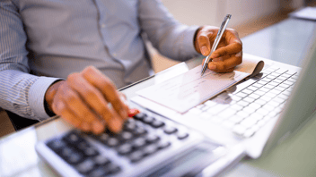 Primer plano de un profesional usando una calculadora y pluma para el cálculo de la nómina, representando la gestión de un proveedor de maquila de nómina.