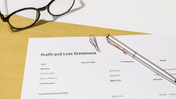 Un Estado de Pérdidas y Ganancias impreso, con un bolígrafo y gafas de lectura, que representa el análisis financiero de utilidades para el cumplimiento de PTU en Recursos Humanos en México.