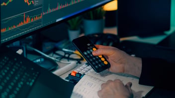 ontador o administrador realizando una auditoría de cumplimiento laboral utilizando una calculadora en su smartphone, frente a monitores con gráficas de nómina y un cuaderno de notas para prevenir multas de la STPS.