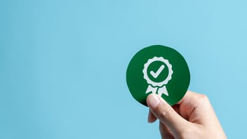 Mano sosteniendo un círculo verde con un ícono blanco de medalla de verificación, simbolizando el éxito de una auditoría interna de nómina en una empresa mexicana.