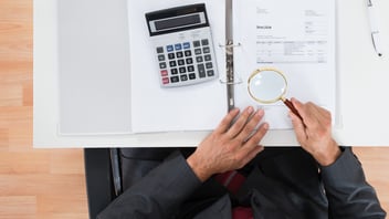 Especialista revisando documentos con lupa y calculadora durante una auditoría de nómina preventiva para detectar discrepancias entre SAT e IMSS.