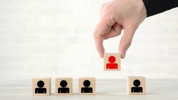 Mano seleccionando un bloque de madera con un icono de persona roja de una fila de bloques, ilustrando el proceso de decisión en una terminación laboral entre finiquito y liquidación.