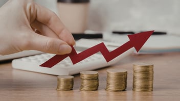 Mano sosteniendo una flecha roja de crecimiento ascendente sobre pilas de monedas y una calculadora de fondo, representando la proyección de flujo de efectivo para el reparto de utilidades (PTU).