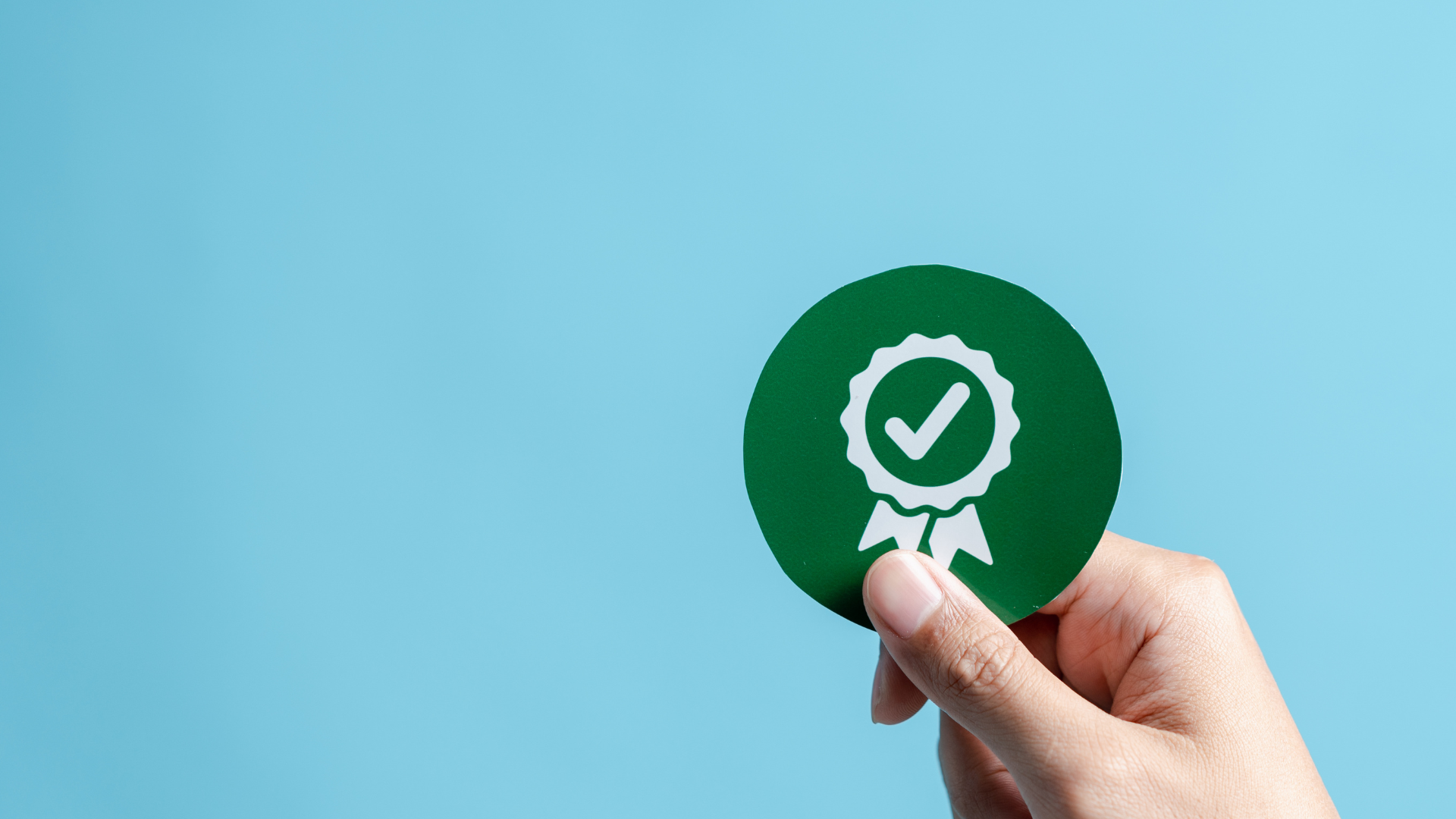 Mano sosteniendo un círculo verde con un ícono blanco de medalla de verificación, simbolizando el éxito de una auditoría interna de nómina en una empresa mexicana.