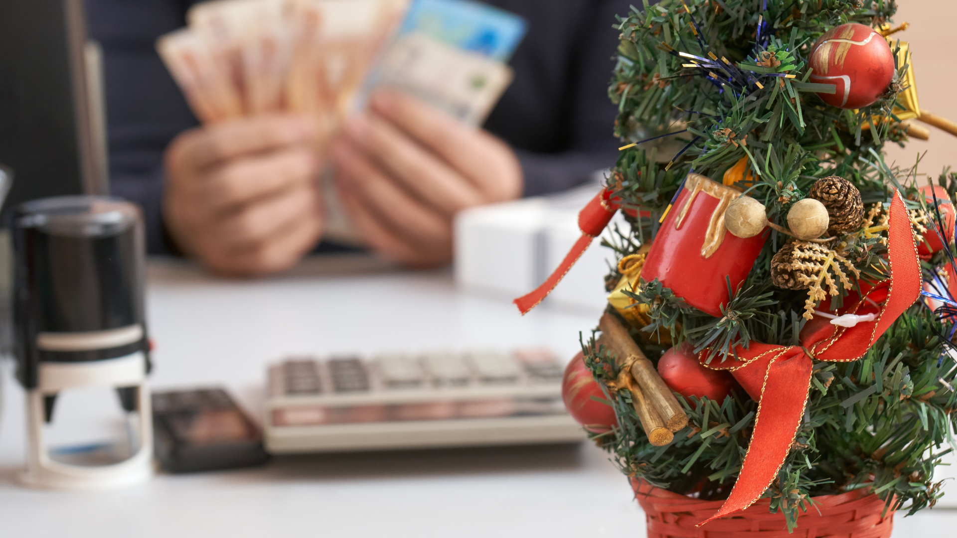 Cálculo de aguinaldo para el pago a trabajadores en México. En primer plano un árbol de Navidad decorado; al fondo, borroso, un empleado contando billetes en una oficina con calculadora y sello.