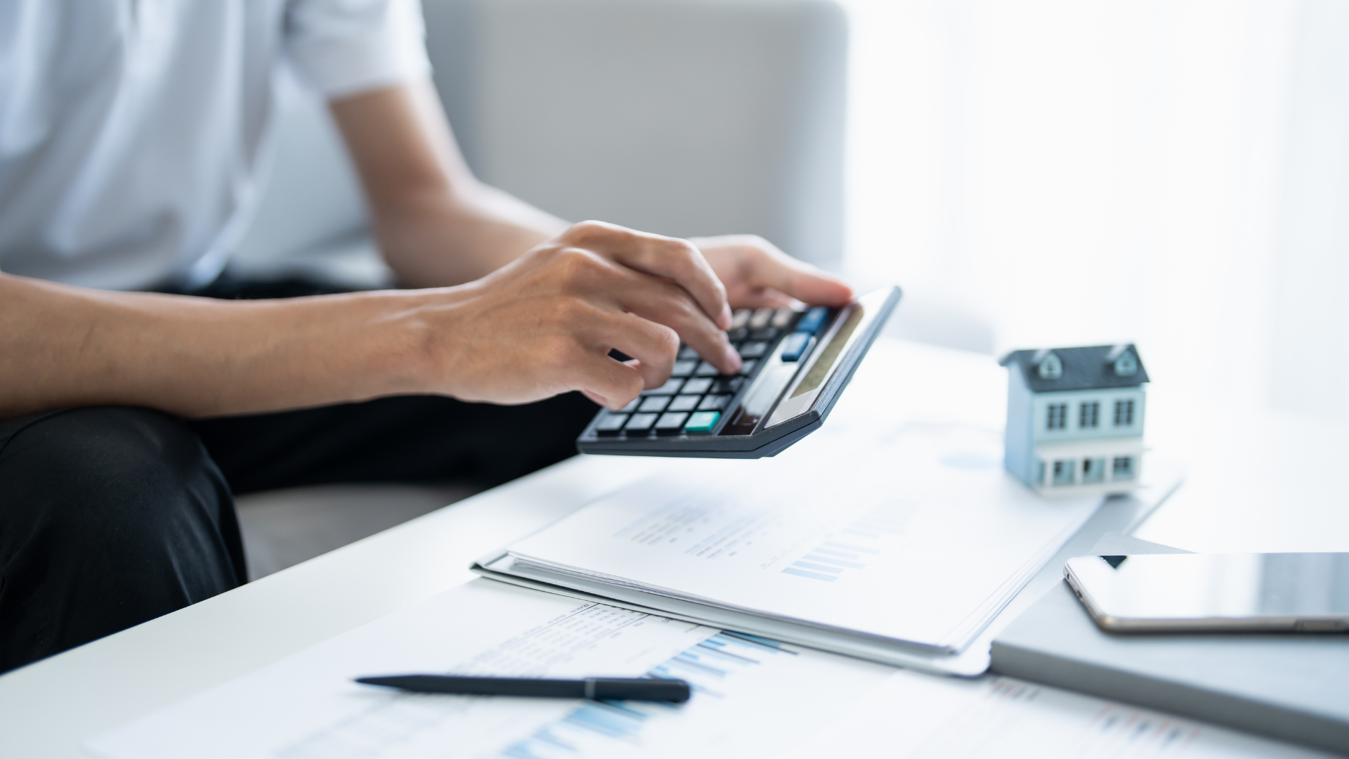 Hombre usando calculadora para calcular el reparto de utilidades PTU 2026 en México con documentos financieros y modelo de casa.